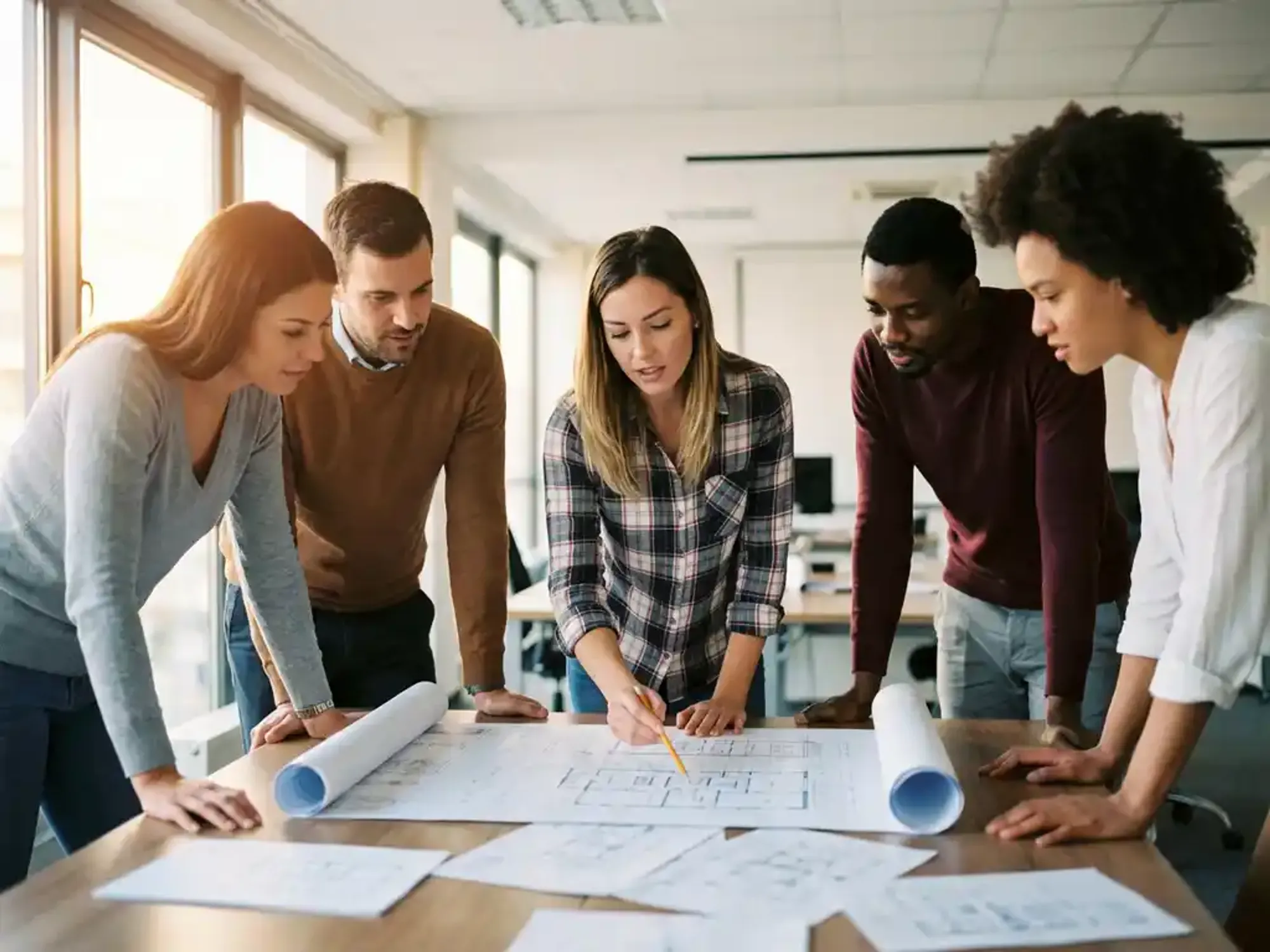 Ingenieur wijst naar technische blauwdruk terwijl divers team samenwerkt rond moderne conferentietafel in kantoor